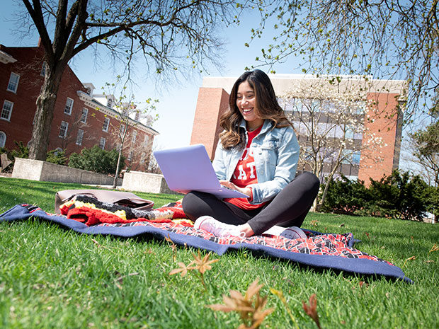 Female student sitting on the quad, working on a laptop.